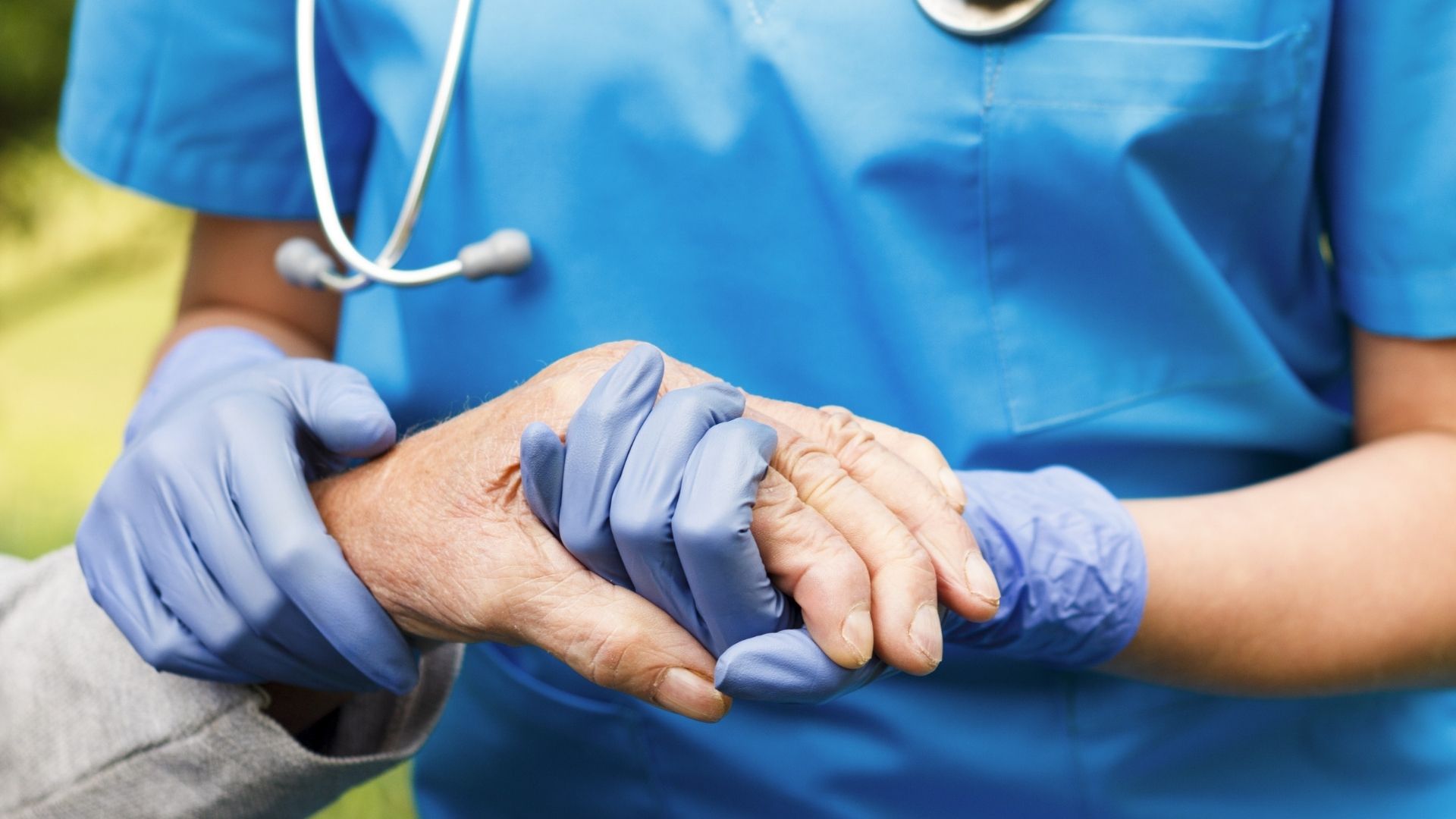 Sjukvårdspersonal håller äldre persons hand. S hotar lägga ner privata vårdgivare i Stockholm.